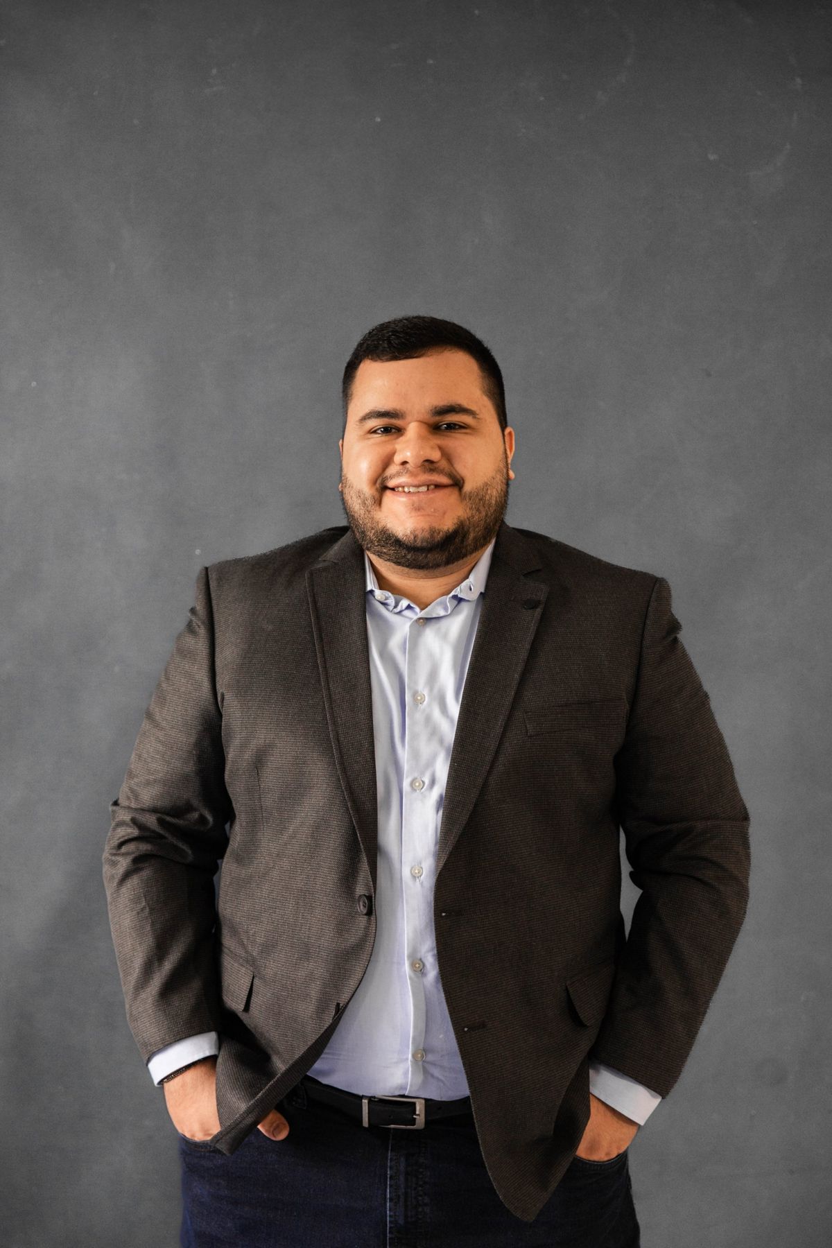 Dr. Lucas Araújo sorrindo, de blazer, em fundo cinza